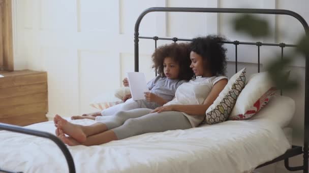 Focused african child daughter reading book on bed with mother — Wideo stockowe