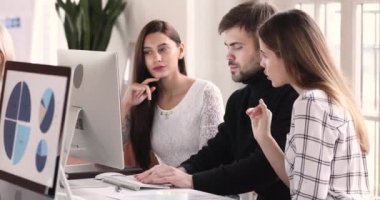 Young male employee helping two female colleagues with computer software.