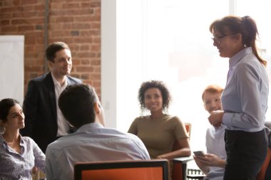 Smiling businesswoman in glasses holding briefing with diverse employees