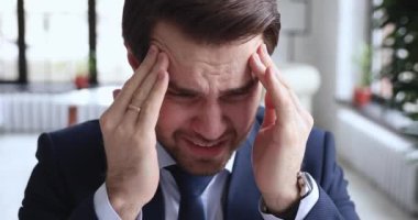 Unhealthy 30s businessman suffering from severe headache in office.