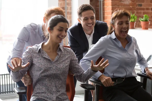 Heureux employés diversifiés s'amuser, monter sur des chaises de bureau — Photo