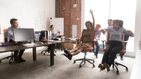 Diversos colegas felices divirtiéndose juntos, montando en silla de oficina —  Fotos de Stock