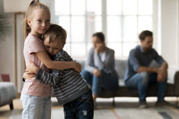 Upset little girl and boy hugging, suffering from parents quarrel
