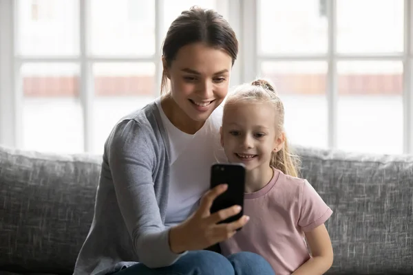 Sorrindo jovem mãe e filha usando smartphone juntos — Fotografia de Stock