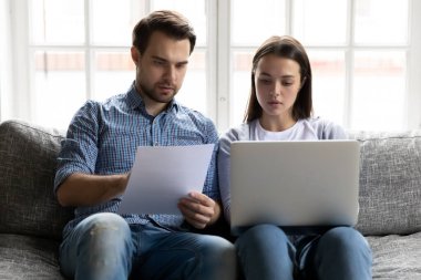 Serious young couple checking financial documents, using online banking service