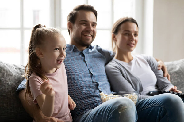 Happy parents with little daughter watching tv together