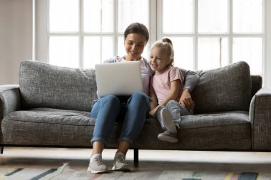 Smiling mother and little daughter hugging, using laptop at home