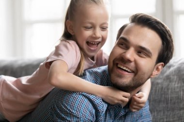 Cute girl lying on happy father back on couch