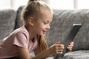 Close up little girl using computer tablet, lying on couch