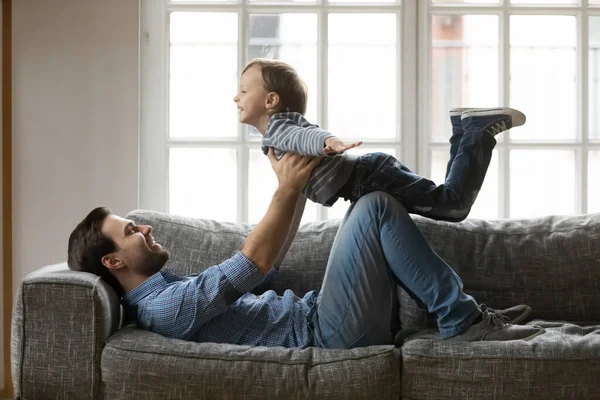 Happy father and little son playing funny game on couch — Stok fotoğraf