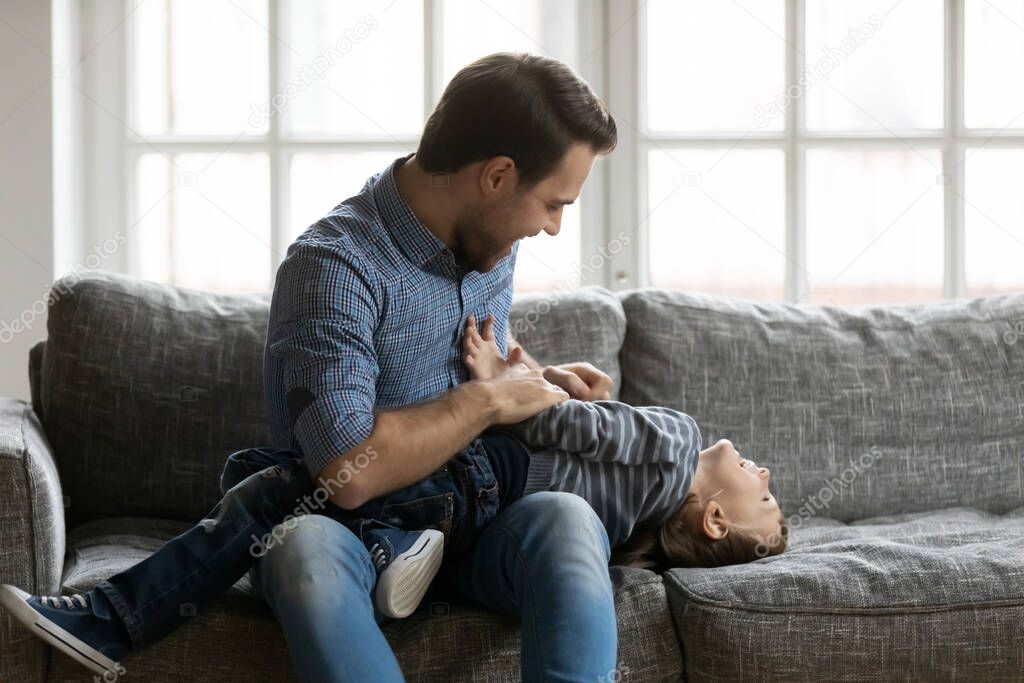 Happy father tickling little adorable son on couch at home