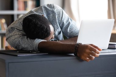 Overworked African employee sleeps at workplace desk