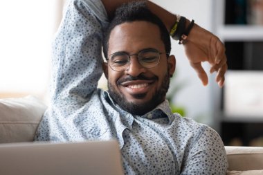 African fellow resting lying on couch using computer watching movie