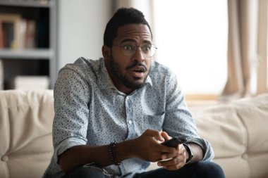 African guy holding remote control watching movie feels appalled