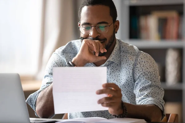 African man sitting at desk reading letter feels satisfied — Stock Photo, Image