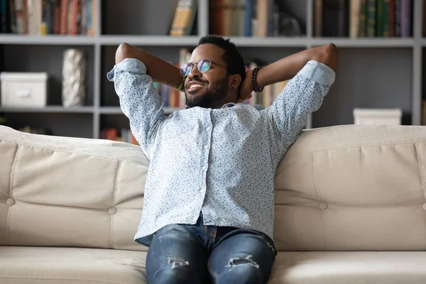 Peaceful African man leaned on couch relaxing looking at window — стокове фото