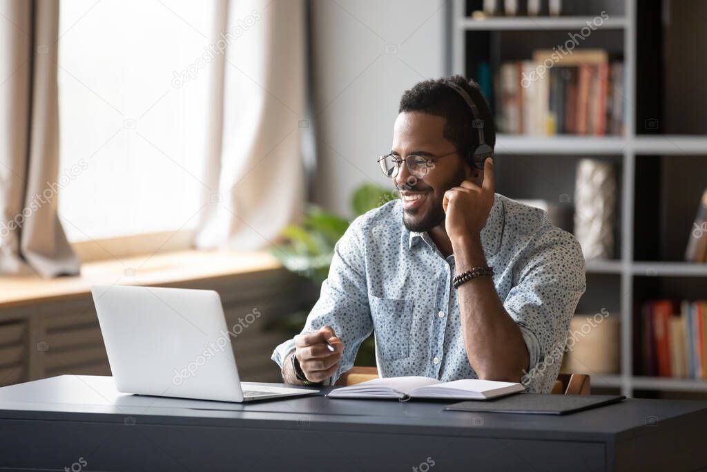 African guy learn online wearing headset looking at laptop screen