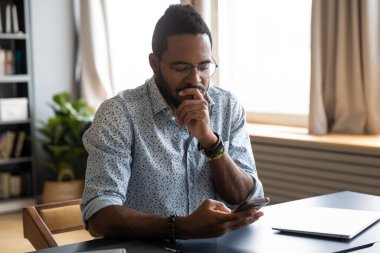 African guy holding smartphone feels concerned thinking over received message