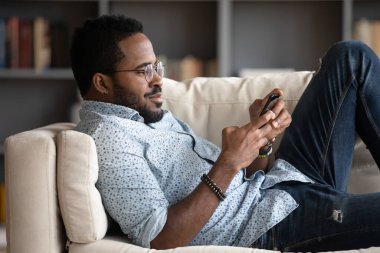 African man lie on couch holding smartphone read media news