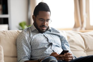 Absorbed african guy read internet news using smartphone at home