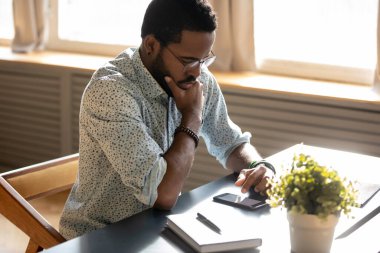 Serious African man read message on smartphone looks focused
