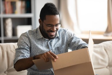 African man opening parcel seated on couch at home