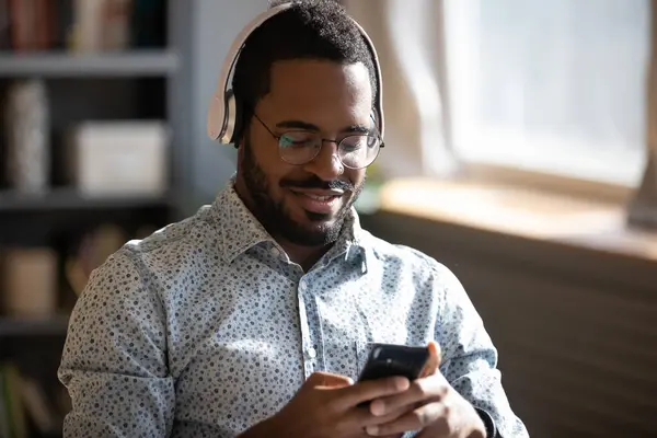 Homem africano usar fones de ouvido detém celular ouve música favorita — Fotografia de Stock