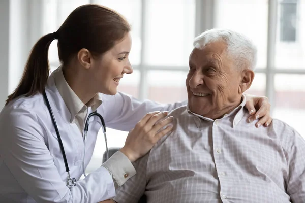 Medico badante femminile che sostiene l'uomo anziano sorridente, toccando le spalle — Foto Stock