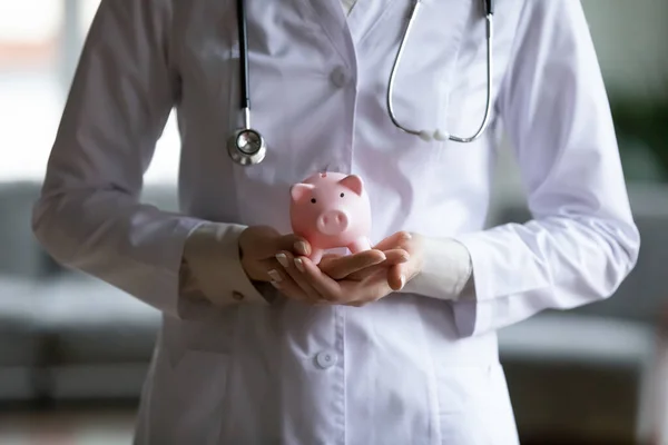 Close up young female doctor holding pink piggy bank — Stock Photo, Image
