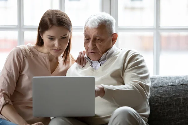 Молодая женщина и пожилой мужчина используют ноутбук вместе дома — стоковое фото