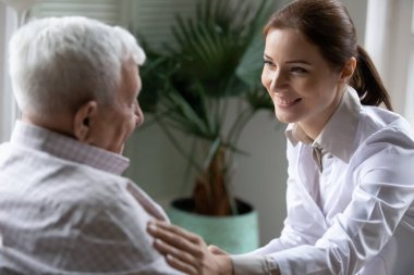Smiling friendly female doctor touching older patient shoulder