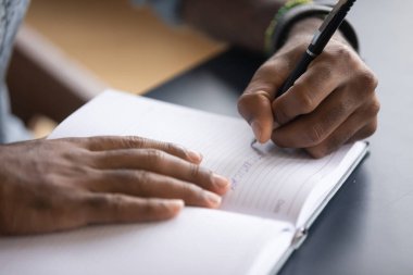 African man seated at desk writes information on notebook closeup