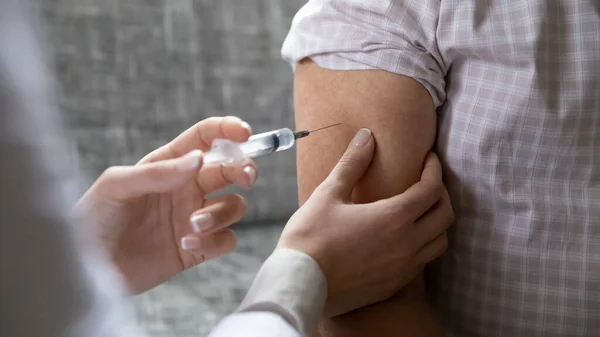 Close up young female nurse vaccinating older man, using syringe — Stockfoto