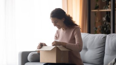 Smiling woman unboxing parcel with online store order, removing package