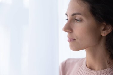 Close up thoughtful young woman looking through window