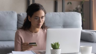 Focused woman wearing glasses paying online by credit card