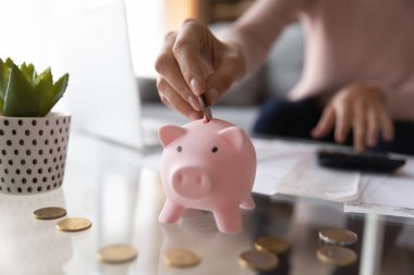 Close up woman putting coin in piggy bank, calculating bills