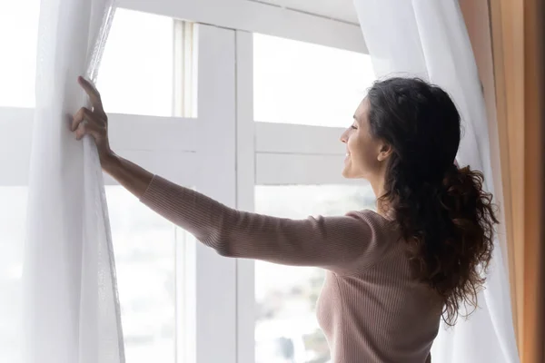 De cerca mujer sonriente abriendo cortinas en la mañana, disfrutando de la luz del sol — Foto de Stock