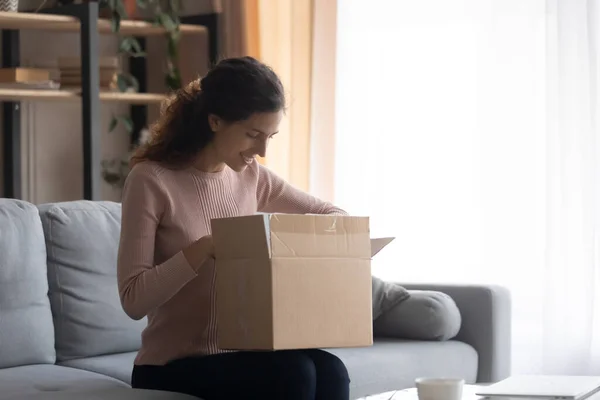 Smiling young woman unpacking cardboard box with internet store order — Stock fotografie