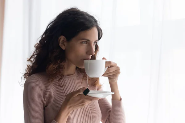 Beautiful young woman drinking tea, looking at window — ストック写真