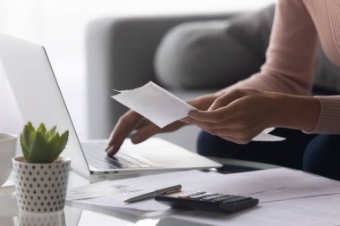 Close up woman holding receipt, using laptop, calculating bills