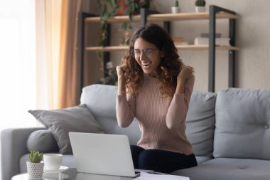 Overjoyed woman wearing glasses celebrating success, online win