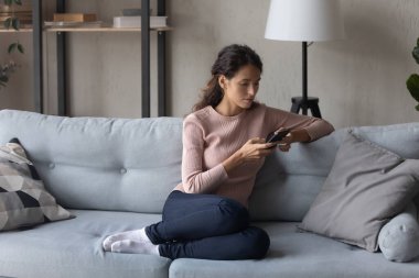 Peaceful young woman relaxing on couch, using smartphone