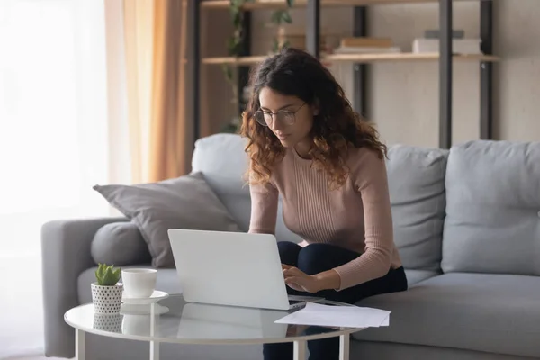 Serious woman wearing glasses working on laptop in living room — Stock fotografie