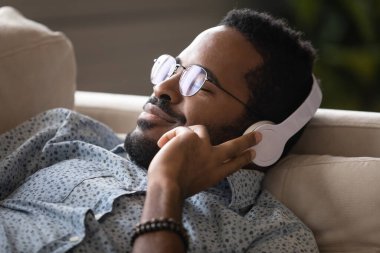 Closeup face of african guy wearing headphones relaxing listening music