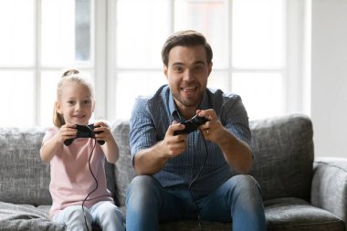 Happy father and adorable daughter playing video game, holding gamepads