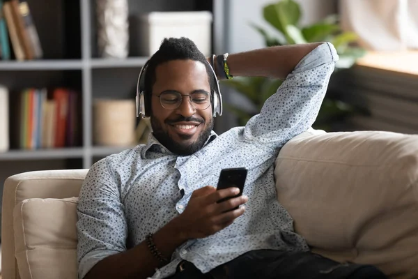 Africano cara segurando celular escuta música através de fones de ouvido sem fio — Fotografia de Stock