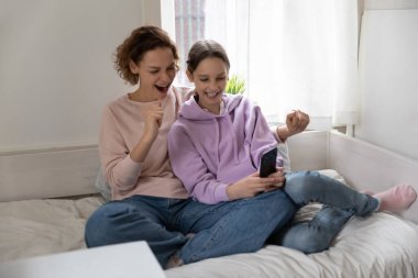 Happy mother and teen daughter using cellphone together