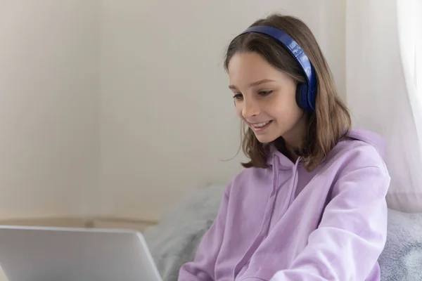 Smiling teenager in headphones using laptop at home — Stock Photo, Image