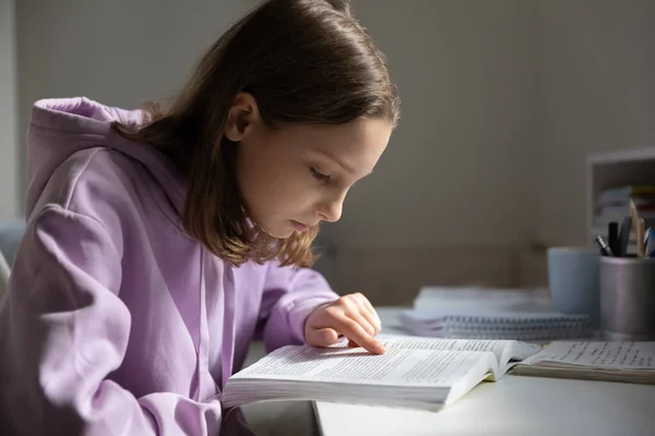 Focused schoolgirl reading book studying at home — Stockfoto